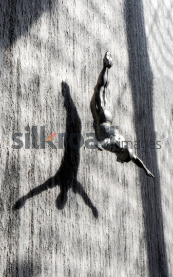Silver Diver Sculpture Against Waterfall with Dramatic Shadow