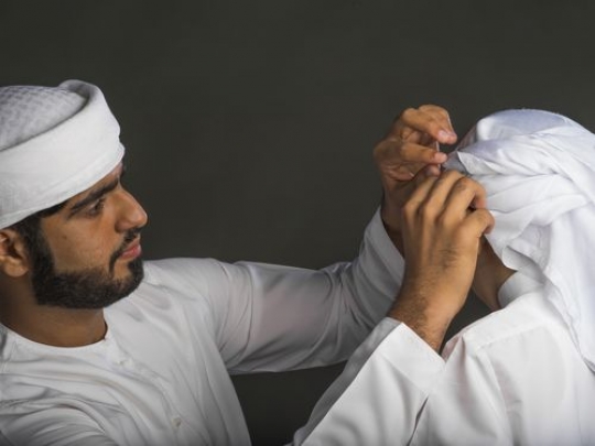 Middle Eastern Man fixing the young boy's traditional attire|