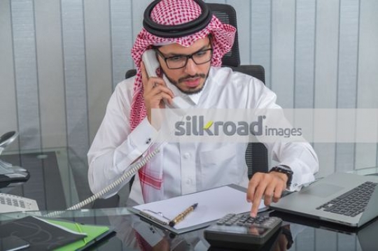 Businessman using calculator talking on the phone 