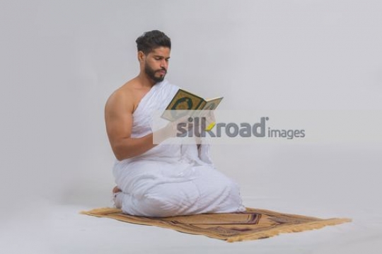 Middle eastern man dressed in the religious attire reading the Quran|